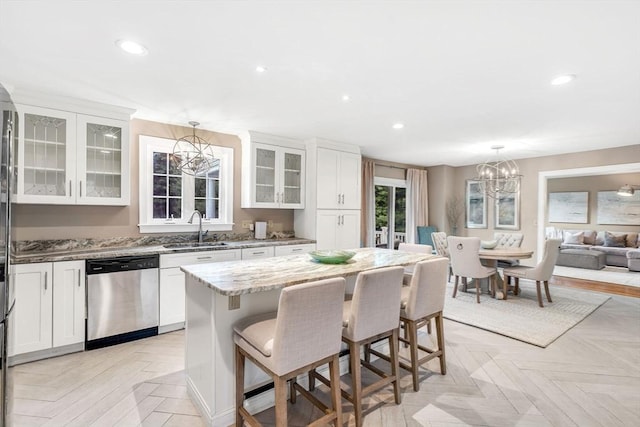 kitchen with light stone countertops, dishwasher, sink, decorative light fixtures, and a kitchen island