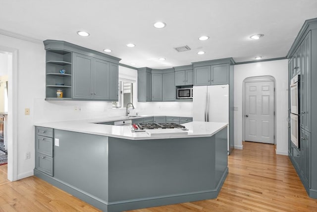 kitchen with light wood-style floors, appliances with stainless steel finishes, crown molding, and a peninsula