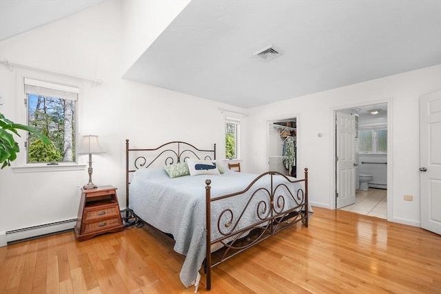 bedroom with a walk in closet, visible vents, a baseboard radiator, connected bathroom, and light wood-style flooring