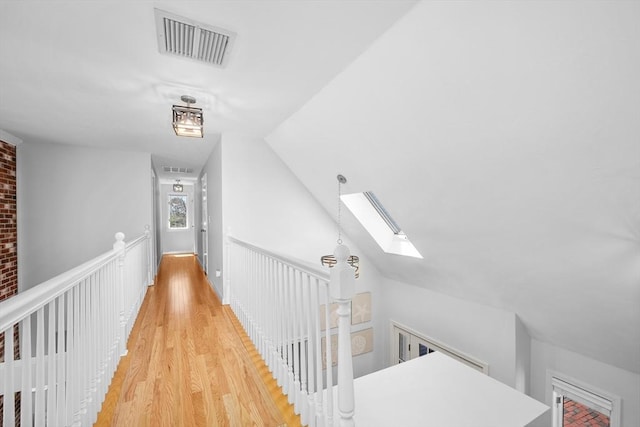corridor with visible vents, light wood-style flooring, an upstairs landing, and vaulted ceiling with skylight