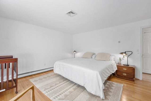 bedroom featuring visible vents, light wood-style flooring, and a baseboard radiator