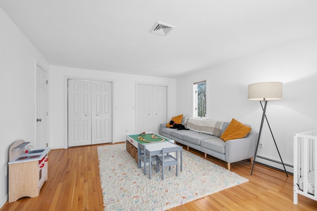 living area with light wood-style floors, baseboard heating, and visible vents