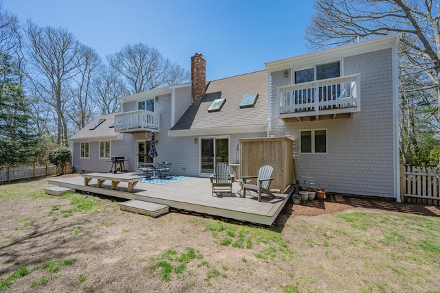 back of property featuring roof with shingles, fence, a balcony, and a chimney