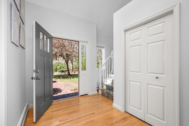 entrance foyer with light wood finished floors, baseboard heating, and stairway