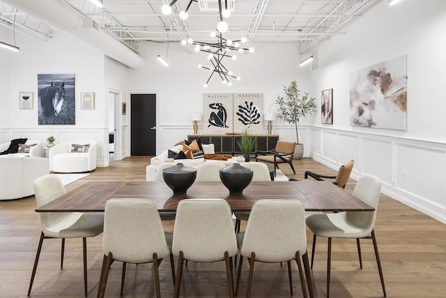 dining area with light wood-type flooring, a notable chandelier, a towering ceiling, and a decorative wall