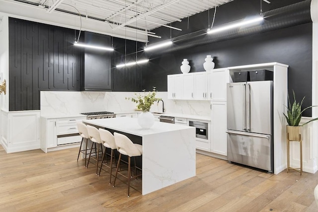 kitchen featuring a kitchen island, a breakfast bar, light wood-style flooring, appliances with stainless steel finishes, and tasteful backsplash