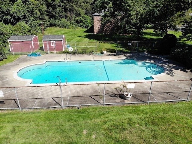 community pool with a storage shed, a yard, fence, and an outdoor structure