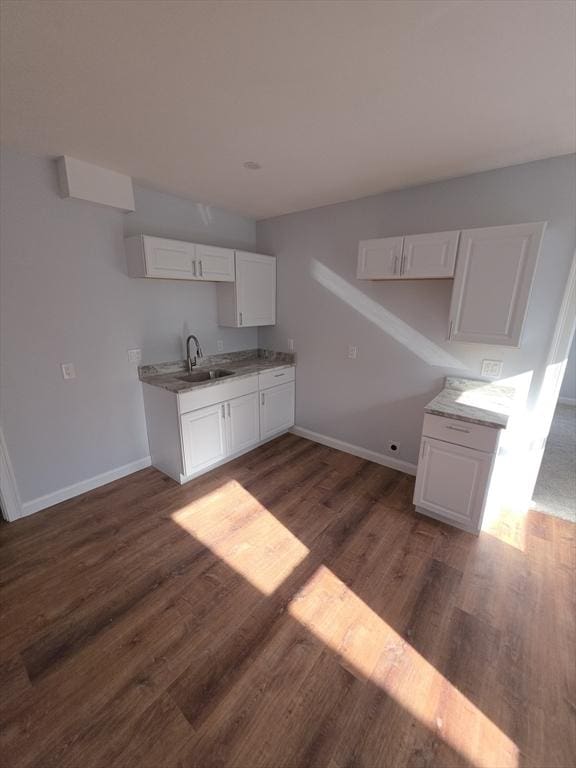 kitchen featuring a sink, wood finished floors, baseboards, and white cabinetry