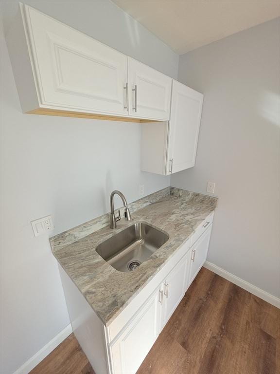 kitchen with a sink, dark wood-style floors, baseboards, and white cabinetry