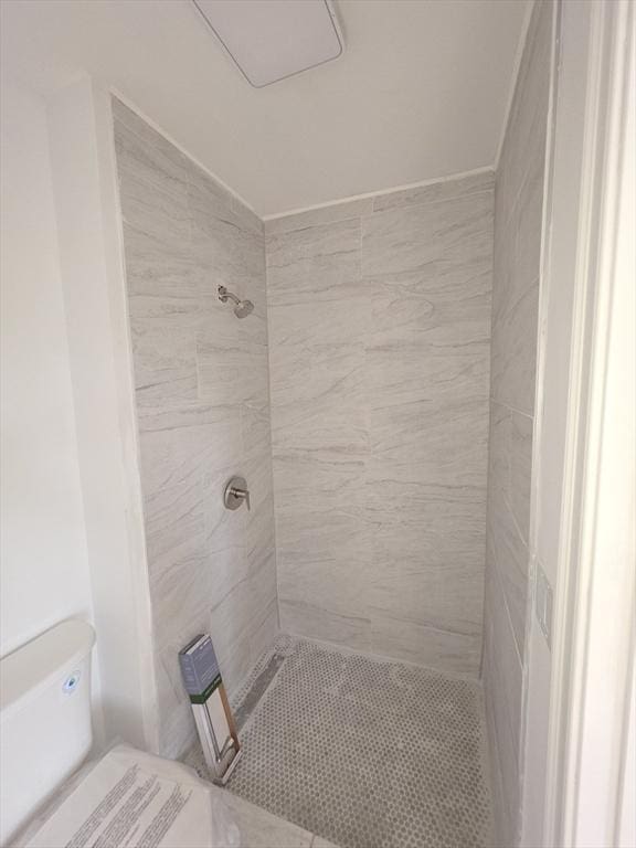 full bathroom featuring tiled shower and toilet