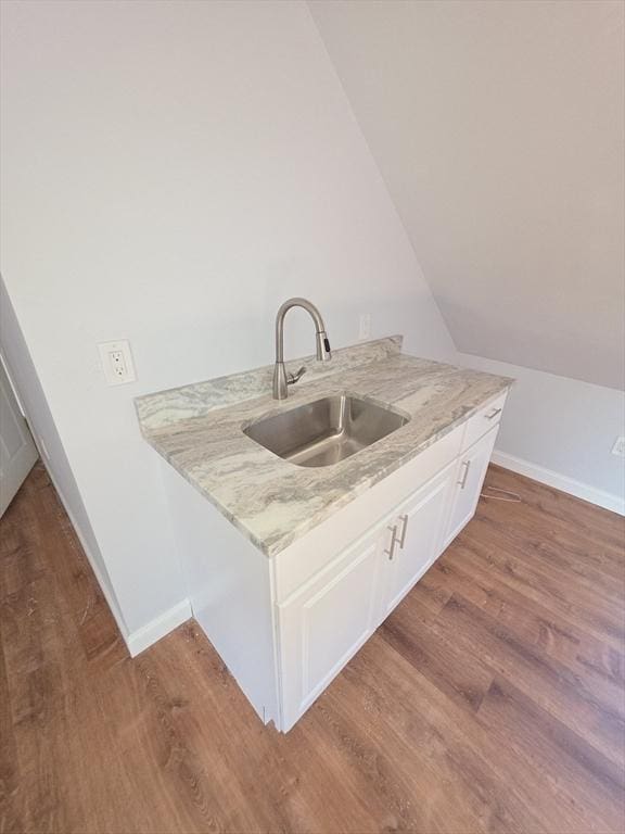 clothes washing area with a sink, wood finished floors, and baseboards