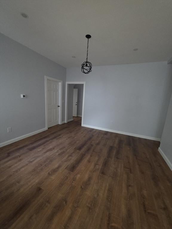 unfurnished dining area with dark wood-style flooring, baseboards, and a chandelier