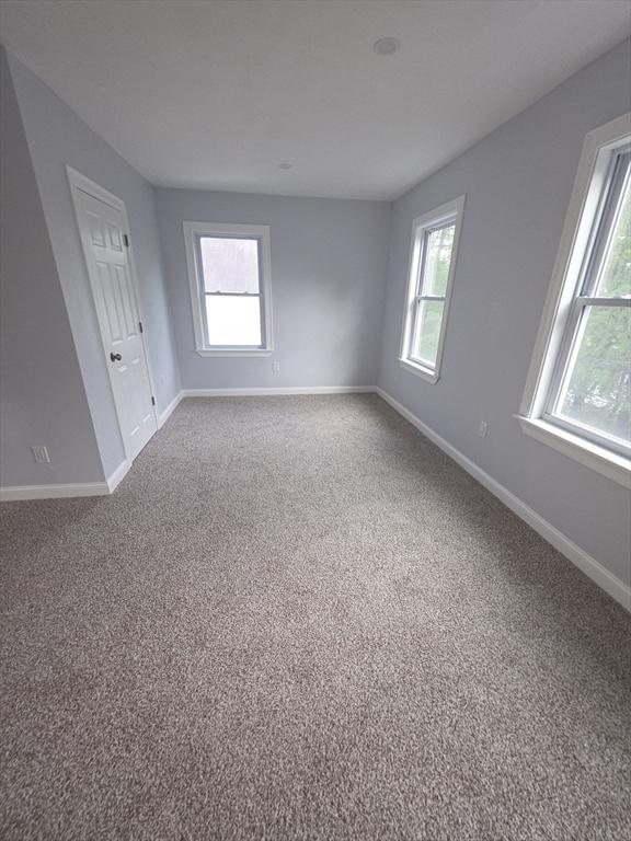 carpeted spare room featuring healthy amount of natural light and baseboards
