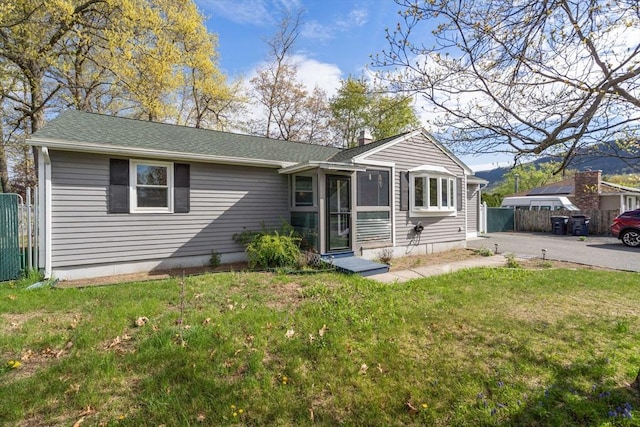 ranch-style house with roof with shingles, fence, a front yard, and a chimney