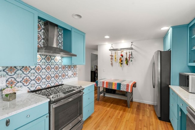 kitchen featuring blue cabinets, tasteful backsplash, light wood-type flooring, stainless steel appliances, and wall chimney exhaust hood
