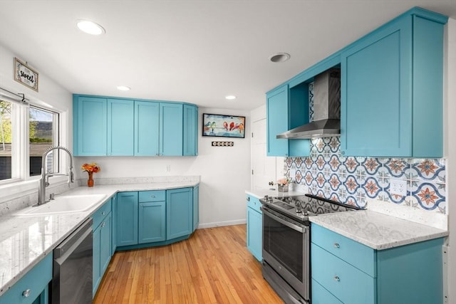 kitchen featuring light wood-style floors, wall chimney exhaust hood, blue cabinets, a sink, and appliances with stainless steel finishes