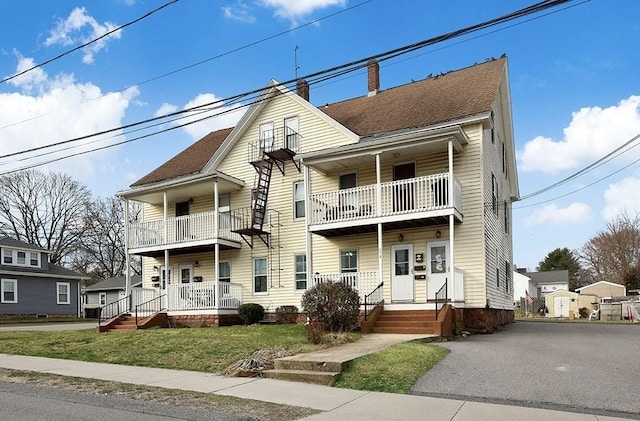 view of front facade with covered porch, a chimney, a front lawn, and a balcony