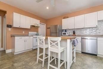 kitchen with decorative backsplash, a kitchen island, a kitchen bar, appliances with stainless steel finishes, and white cabinetry