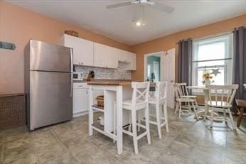 kitchen with freestanding refrigerator, white cabinetry, ceiling fan, and decorative backsplash