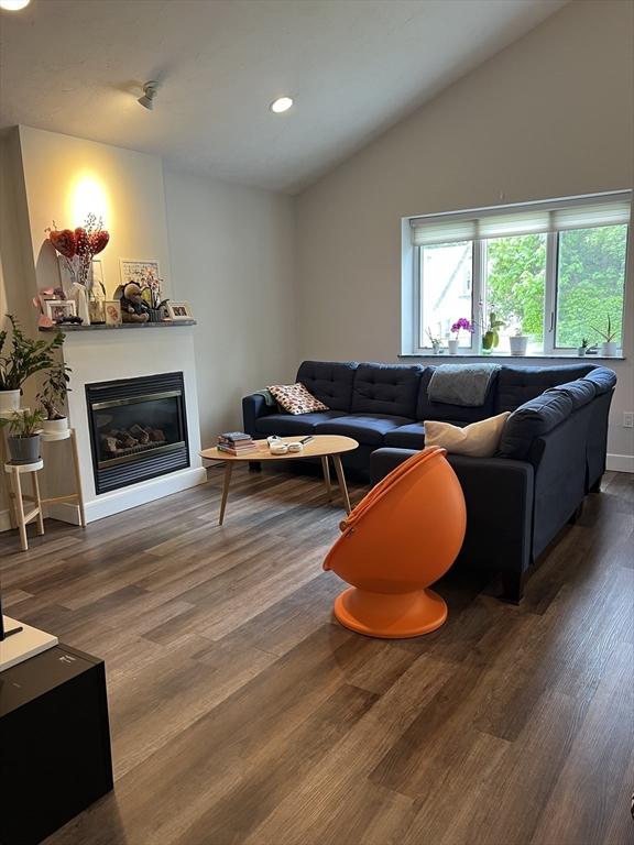 living area featuring wood finished floors, a glass covered fireplace, lofted ceiling, recessed lighting, and baseboards