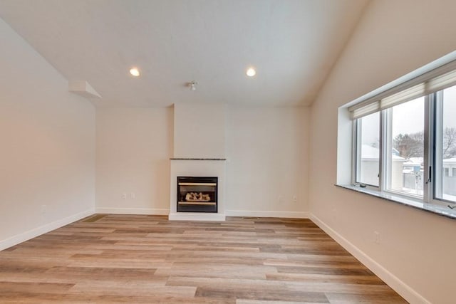 unfurnished living room with a glass covered fireplace, recessed lighting, baseboards, light wood-type flooring, and vaulted ceiling
