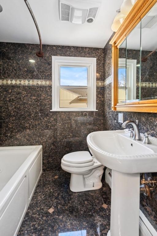 bathroom with a washtub, toilet, and tile walls