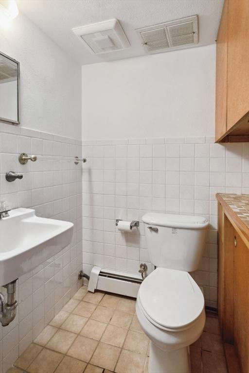 bathroom with tile patterned flooring, a baseboard heating unit, tile walls, and toilet