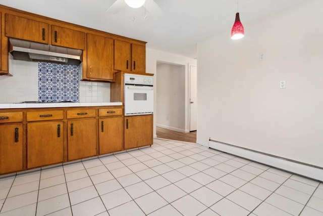 kitchen with pendant lighting, a baseboard heating unit, oven, decorative backsplash, and cooktop