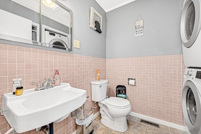 bathroom with tile walls, toilet, sink, and stacked washer / drying machine