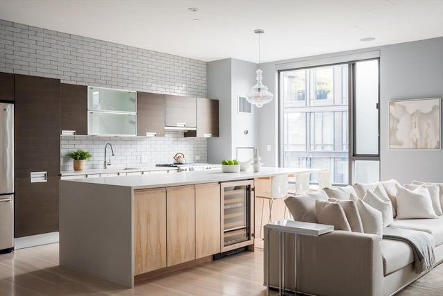 kitchen with decorative light fixtures, light hardwood / wood-style flooring, a kitchen island, beverage cooler, and decorative backsplash