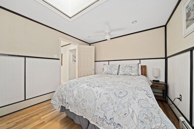 bedroom with baseboard heating, ornamental molding, wood-type flooring, and a skylight