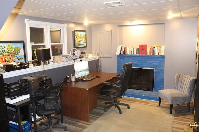 home office with a paneled ceiling, wood-type flooring, and a brick fireplace