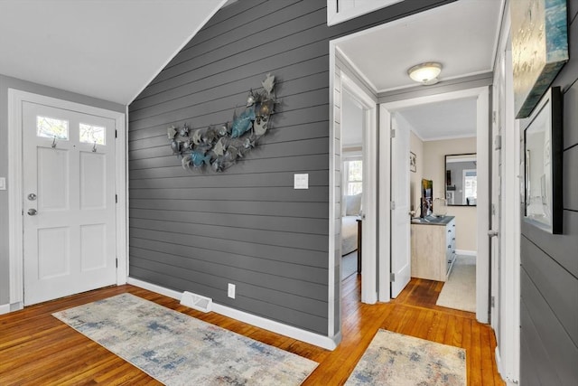 foyer with lofted ceiling, ornamental molding, baseboards, light wood finished floors, and visible vents
