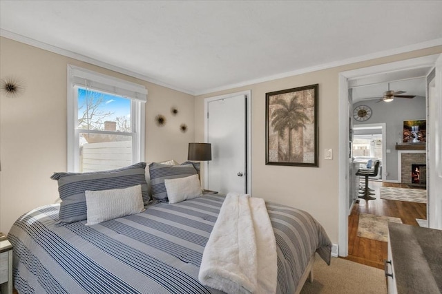 bedroom featuring baseboards, a fireplace, wood finished floors, and crown molding