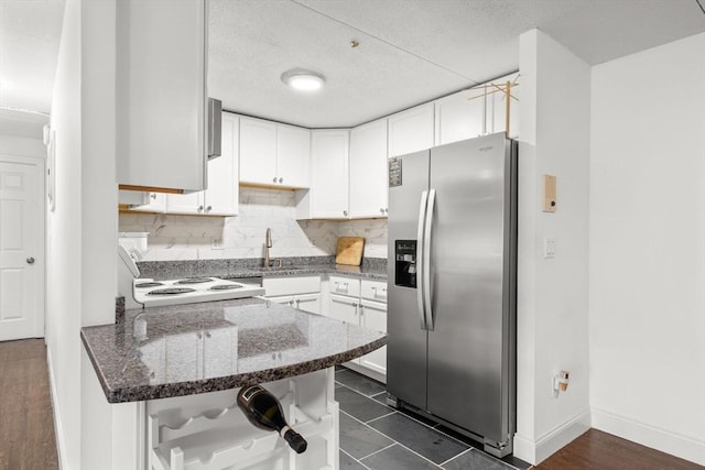 kitchen with stove, stainless steel refrigerator with ice dispenser, tasteful backsplash, white cabinets, and dark stone counters