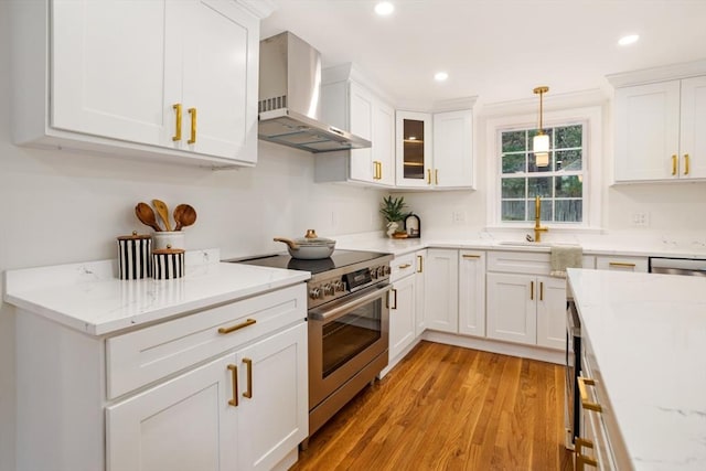 kitchen featuring wall chimney range hood, light wood-style flooring, white cabinetry, light stone countertops, and appliances with stainless steel finishes