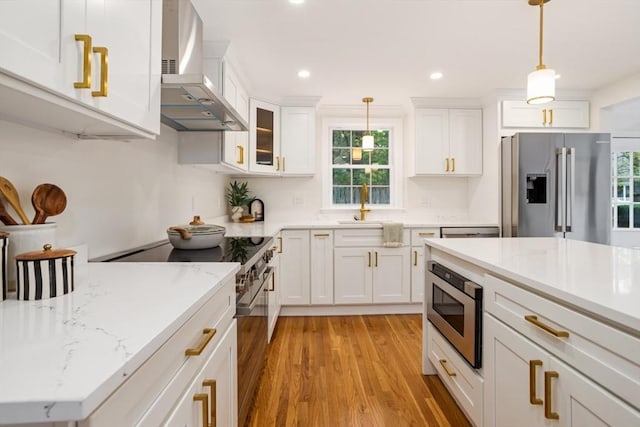 kitchen with wall chimney range hood, light wood-type flooring, premium appliances, and a wealth of natural light