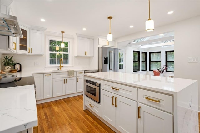 kitchen with appliances with stainless steel finishes, pendant lighting, a sink, white cabinets, and light wood-type flooring