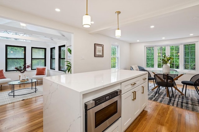 kitchen featuring hanging light fixtures, light wood-type flooring, stainless steel microwave, and white cabinetry