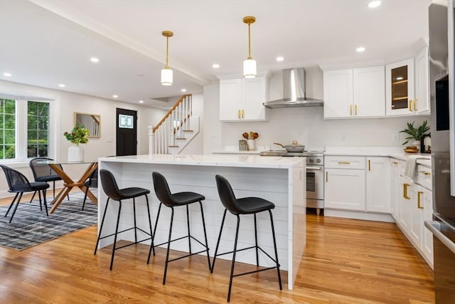 kitchen with wall chimney range hood, a breakfast bar, recessed lighting, stainless steel range, and light wood-style floors