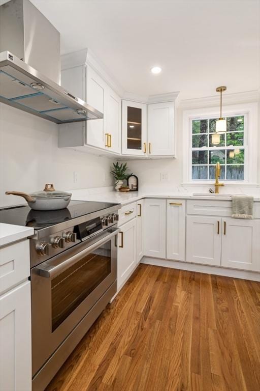 kitchen with a sink, wall chimney range hood, light countertops, and high end stainless steel range