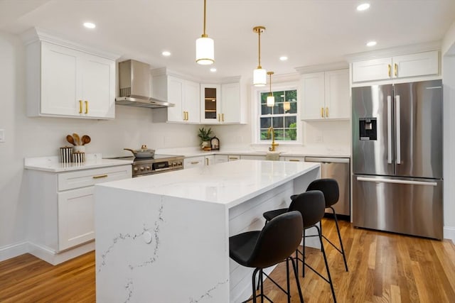 kitchen with light wood-type flooring, appliances with stainless steel finishes, a sink, and wall chimney exhaust hood