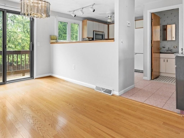 unfurnished dining area with ceiling fan, a chandelier, baseboards, light wood-type flooring, and track lighting