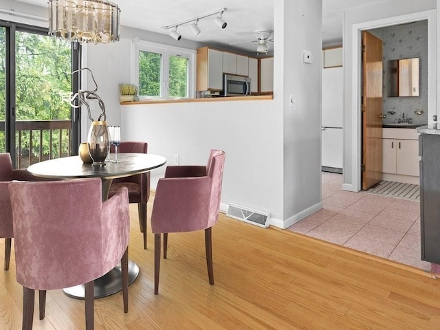 dining room featuring a ceiling fan, light wood finished floors, baseboards, a chandelier, and rail lighting