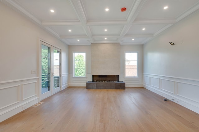 unfurnished living room with beam ceiling, a large fireplace, french doors, coffered ceiling, and light wood-type flooring