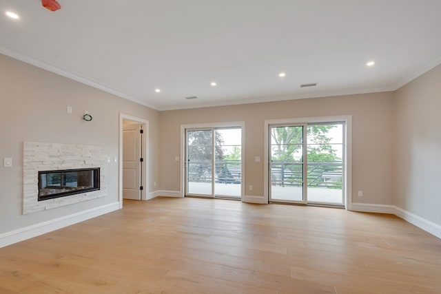 unfurnished living room with light wood-type flooring, a stone fireplace, and ornamental molding