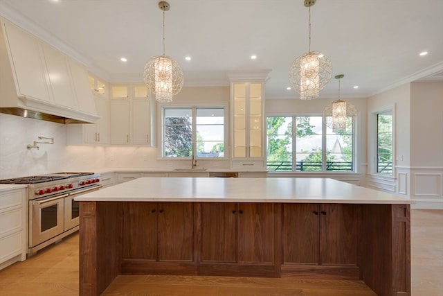 kitchen with range with two ovens, sink, crown molding, a large island, and a chandelier