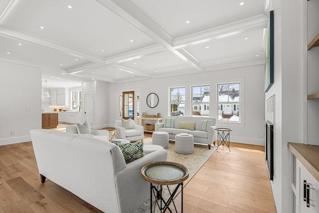 living area featuring ornamental molding, beamed ceiling, a fireplace, and light wood-style flooring