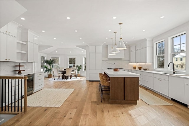 kitchen featuring a center island, light wood-style floors, white cabinets, a sink, and beverage cooler