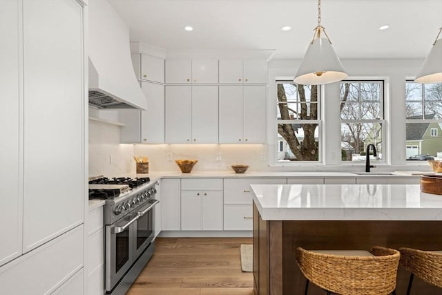 kitchen with premium range hood, a sink, white cabinets, light wood-type flooring, and double oven range